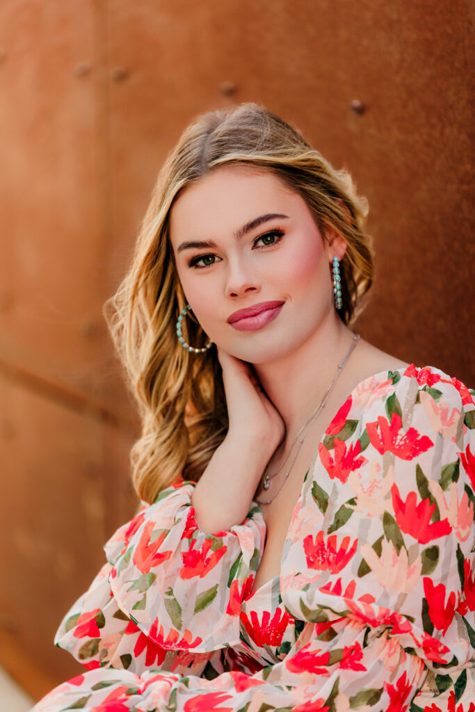senior headshots. senior is wearing red and pink floral top with hand posed on the neck