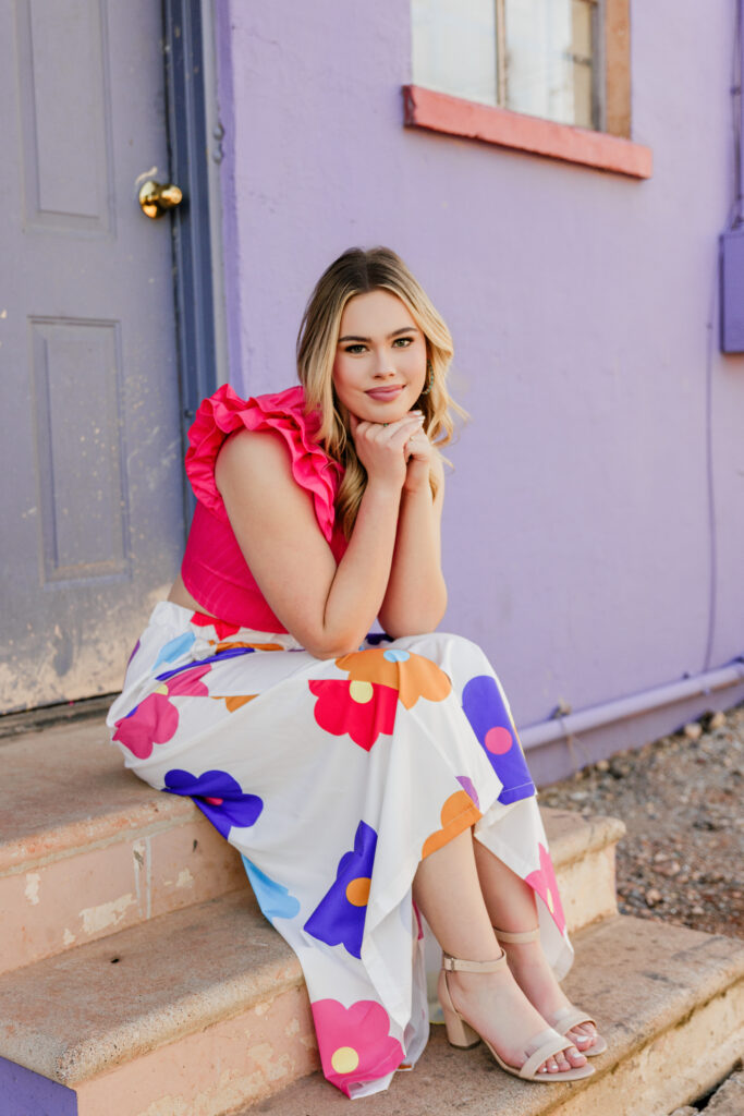 senior photo outfits senior posing with head on hands wearing a pink dressy blouse and a fun floral skirt with chunky heels