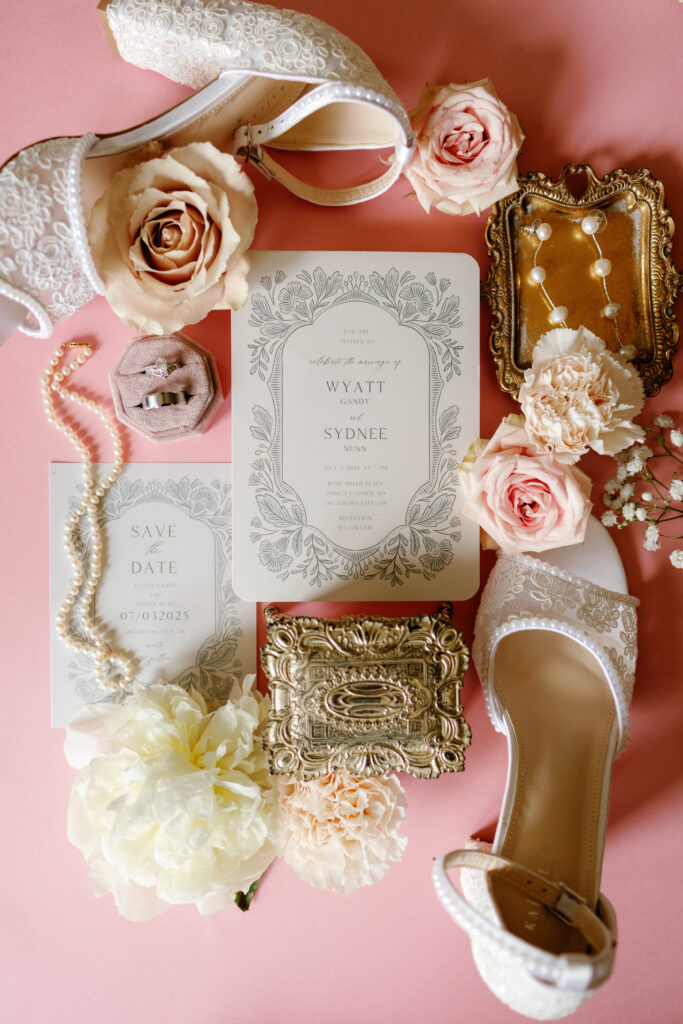Bridal flat lay with wedding invitation, blush florals, jewelry, and heels at Rose Briar Place